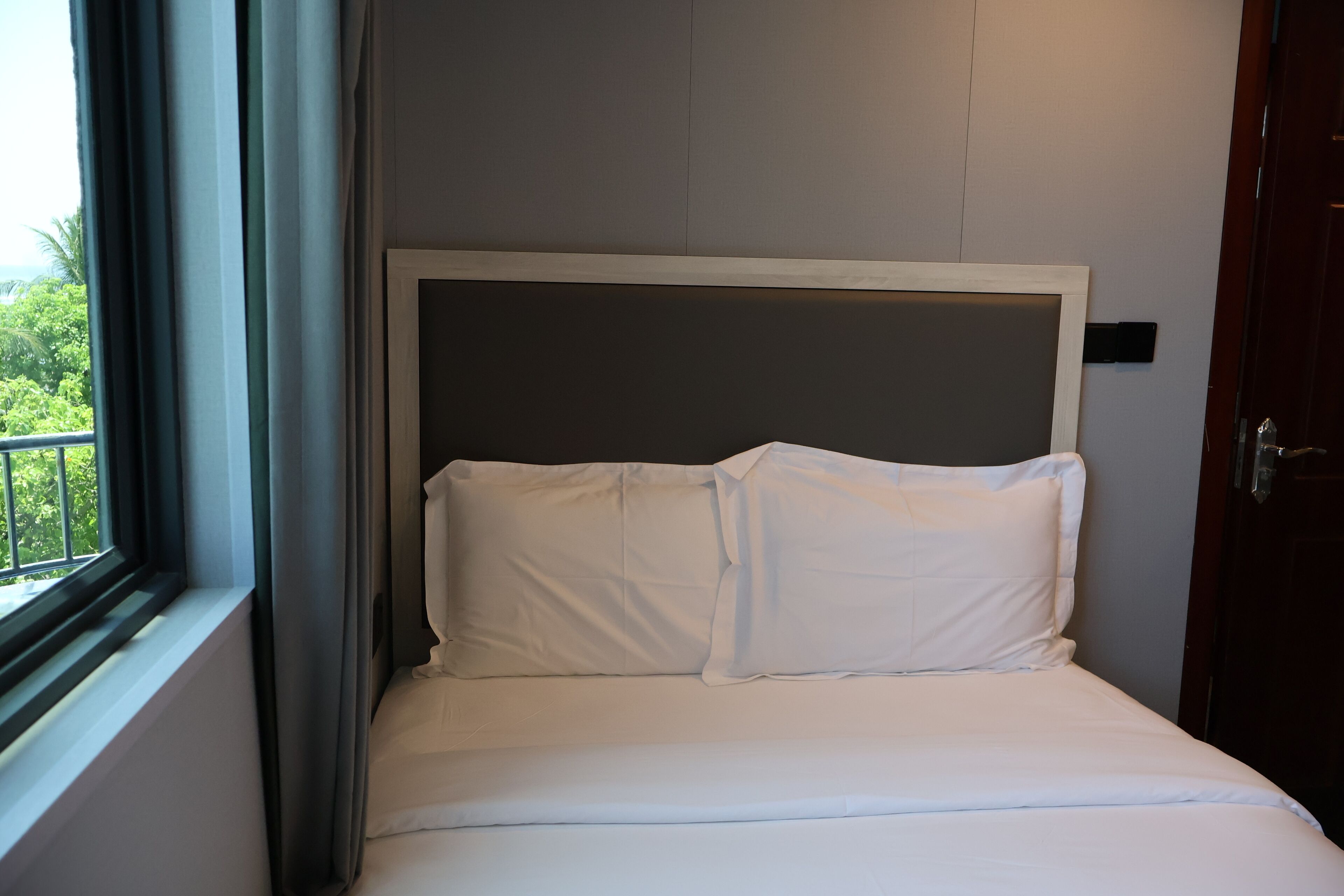 Un lit bien fait, avec du linge de lit blanc, dans une pièce dotée d’une fenêtre et d’une porte.