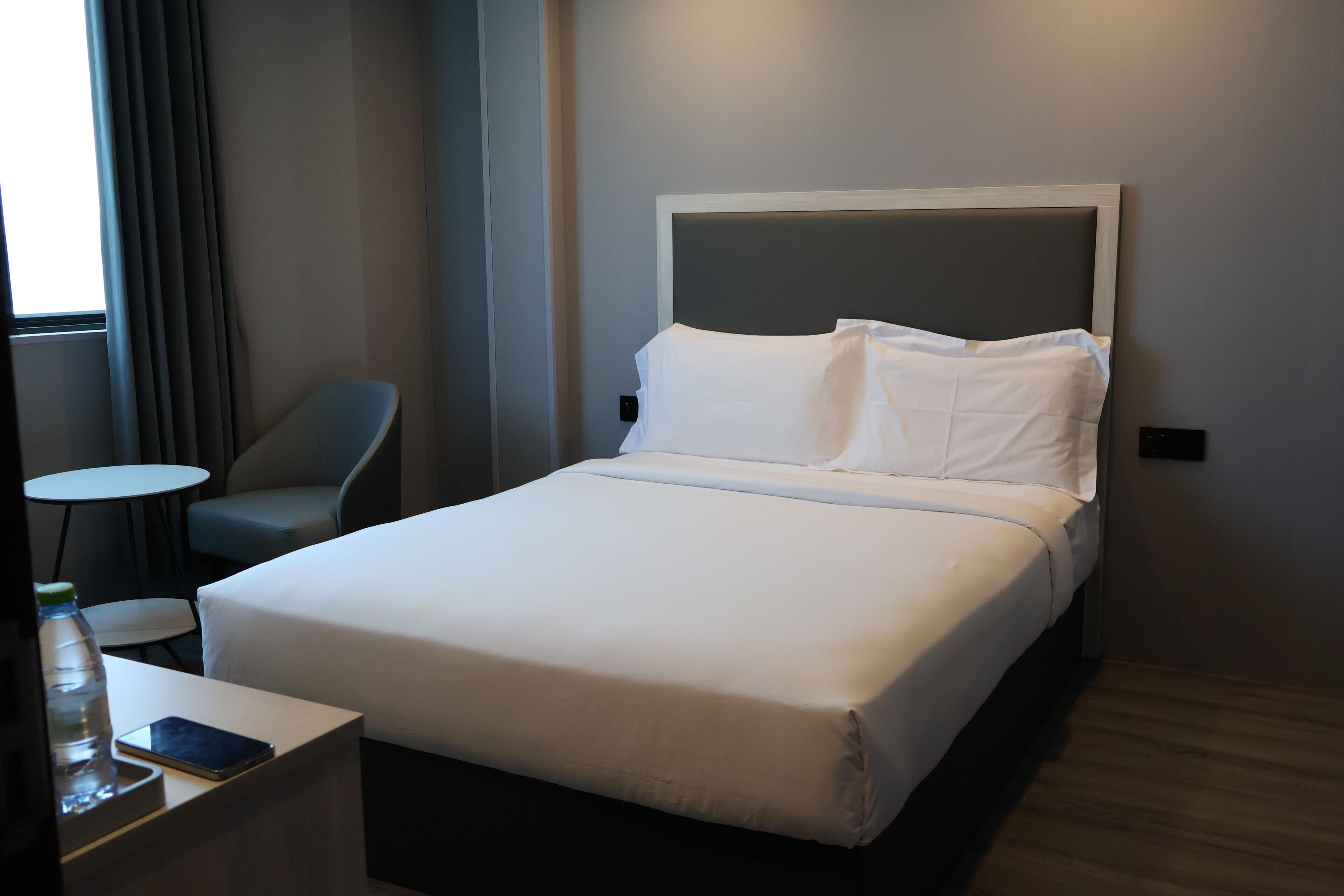 Una habitación de hotel con una cama, una silla, una mesita y una botella de agua.