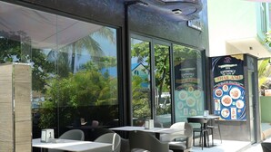 Un espace de restauration en plein air avec des tables et des chaises, un coin salon abrité et une vue sur la rue et la verdure.