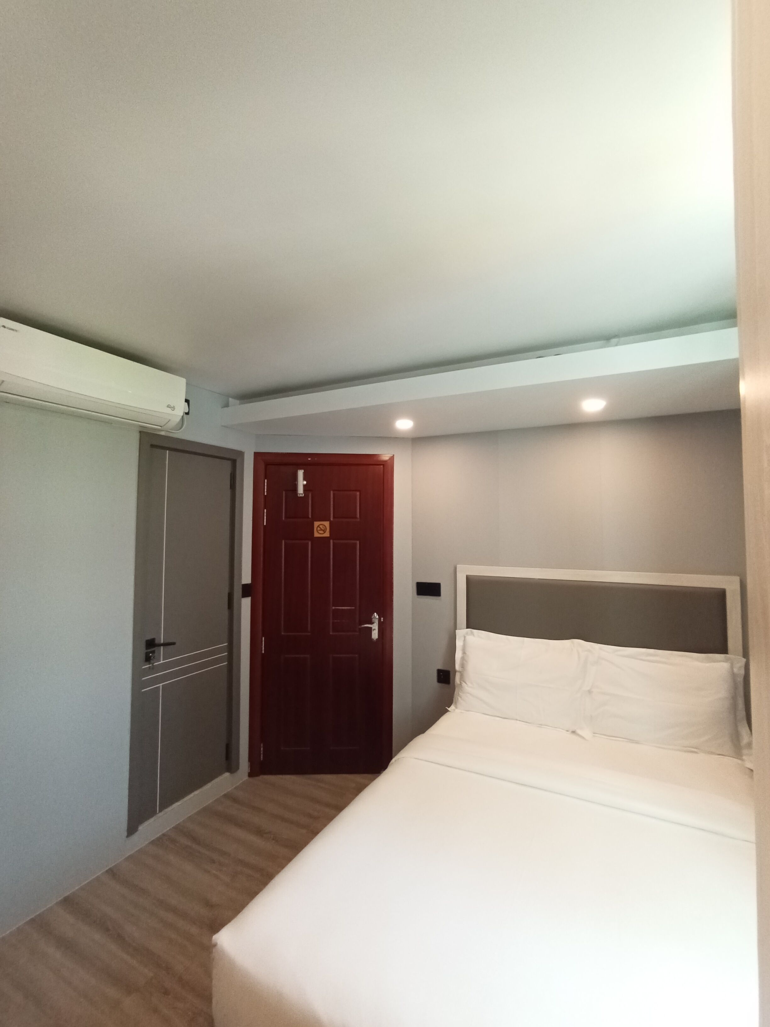 A hotel room with a bed, a wardrobe, a door with a no-smoking sign, and a ceiling light.