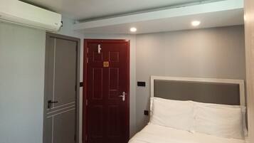 A hotel room with a bed, a wardrobe, a door with a no-smoking sign, and a ceiling light.