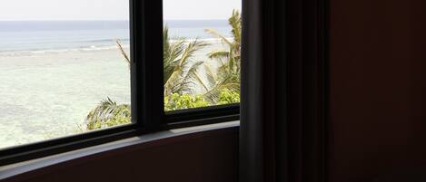 A room with a view of the ocean through a window, a round table, and a curtain.