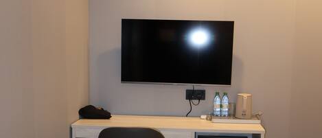 Una habitación de hotel con escritorio, televisor de pantalla plana, una silla y dos camas.