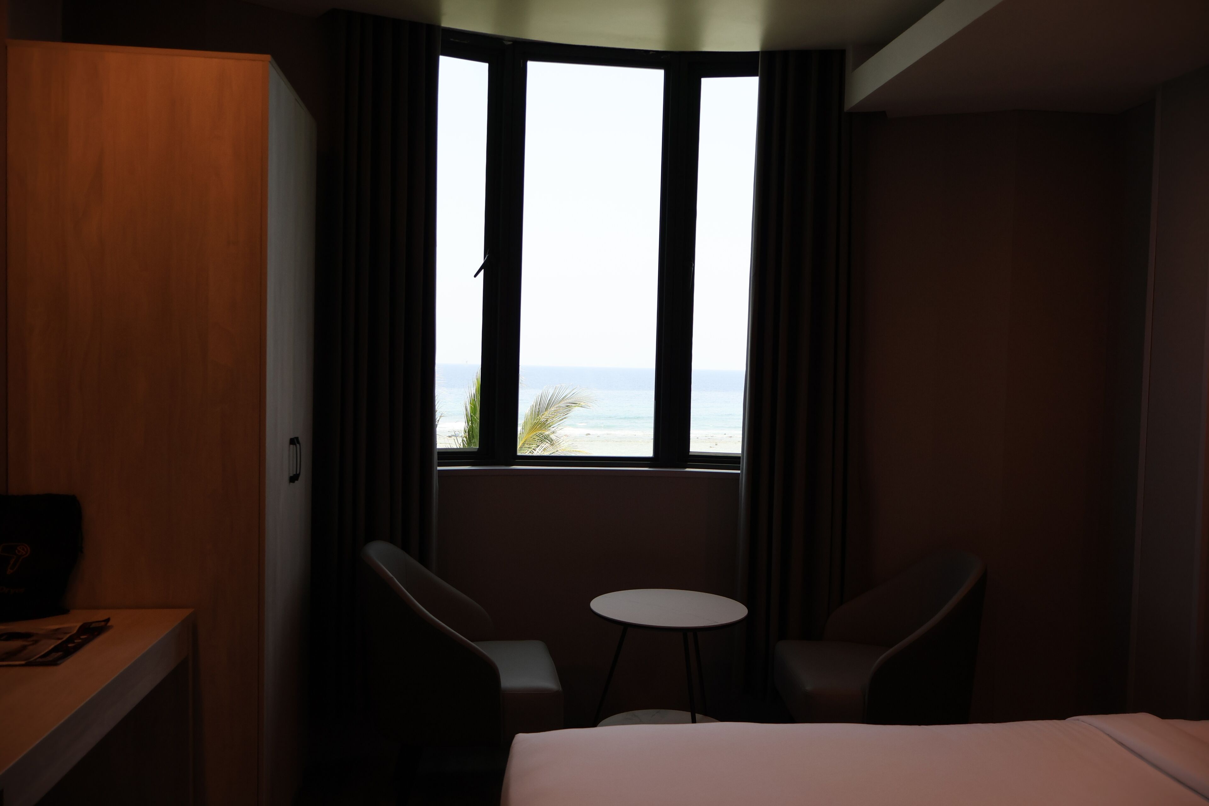 Habitación de hotel con cama, dos sillas, una mesita y ventana con vista a la playa.