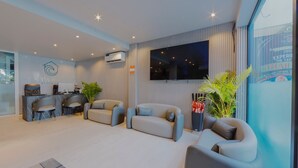 Un hall d’hôtel moderne avec un comptoir d’accueil, un espace salon et un grand écran de télévision.