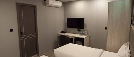 A hotel room with two beds, a desk with a flat-screen TV, an air conditioning unit, and a door.
