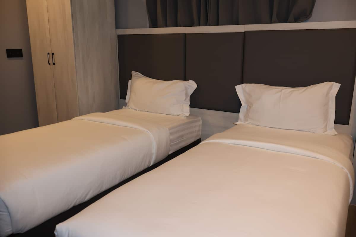 Two single beds with white linens, a wooden wardrobe, and a dark headboard.