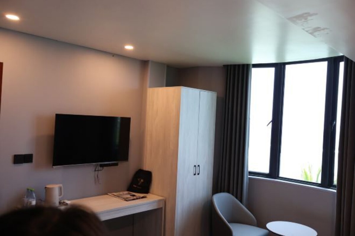 Een hotelkamer met een flatscreen televisie aan de muur, een klein bureau met stoel, een kledingkast en een raam met gordijnen.