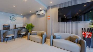 A modern hotel lobby with a reception desk, two sofas, and a large TV screen.