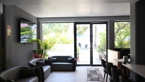 Un hall d’hôtel moderne avec un canapé incurvé, un coin repas et de grandes portes coulissantes en verre donnant sur un patio extérieur.