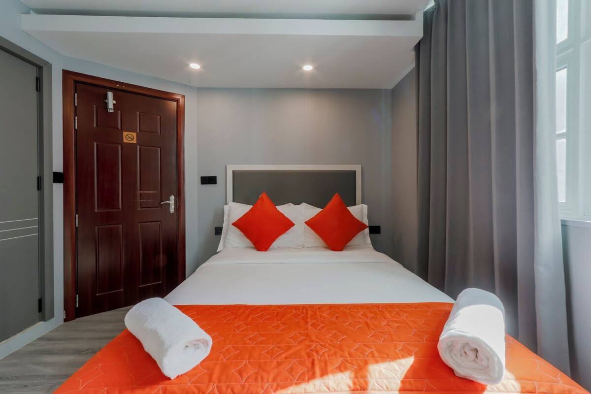 A hotel room with a bed, two red pillows, an orange bedspread, and two rolled towels.