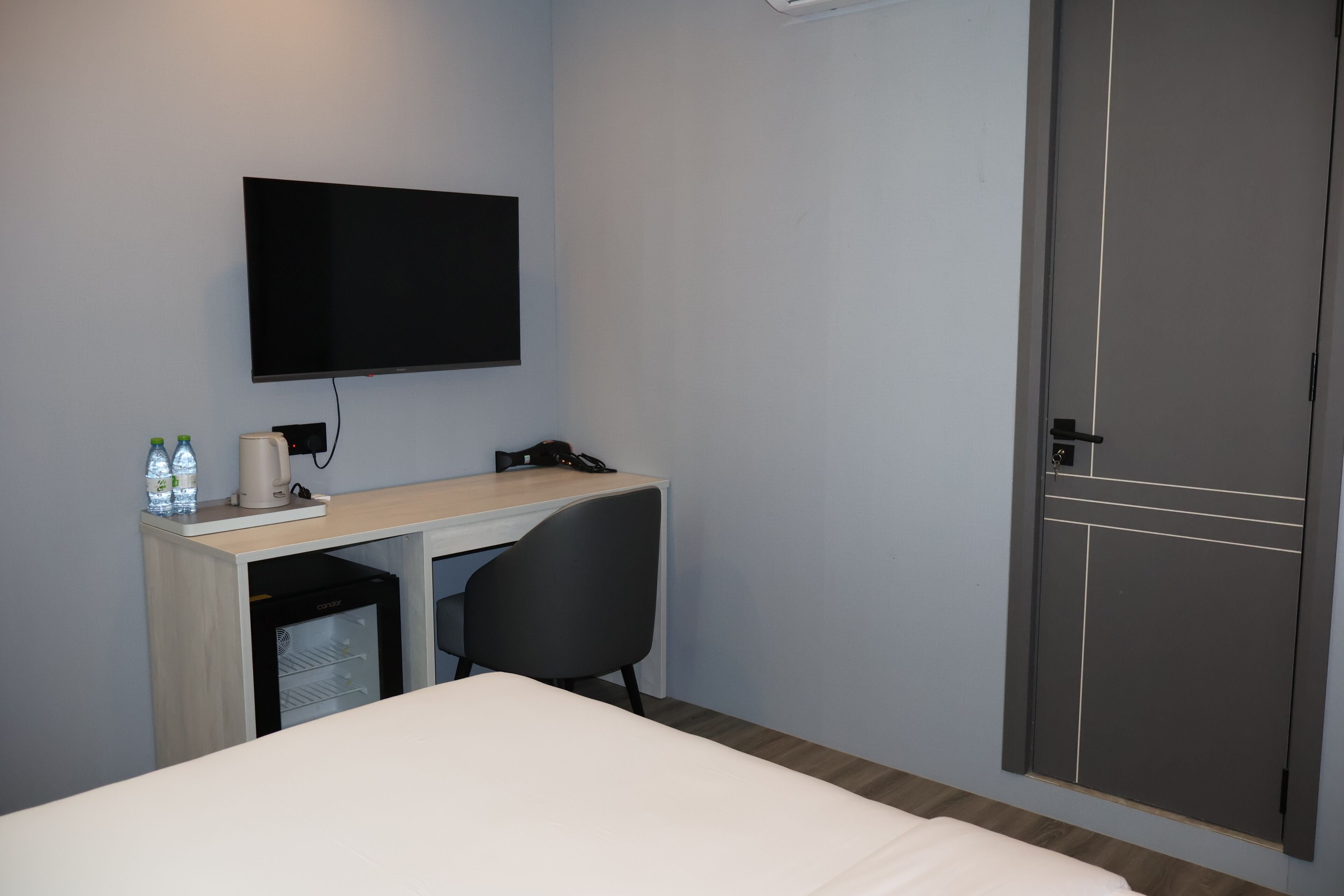 Habitación de hotel con cama, escritorio con ordenador, silla, televisor montado en la pared y un mini bar.