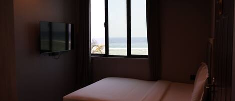 Una habitación de hotel con cama, televisor montado en la pared y un amplio ventanal con vistas al océano.
