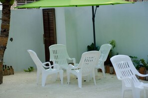 A patio area with white plastic chairs and a green umbrella.