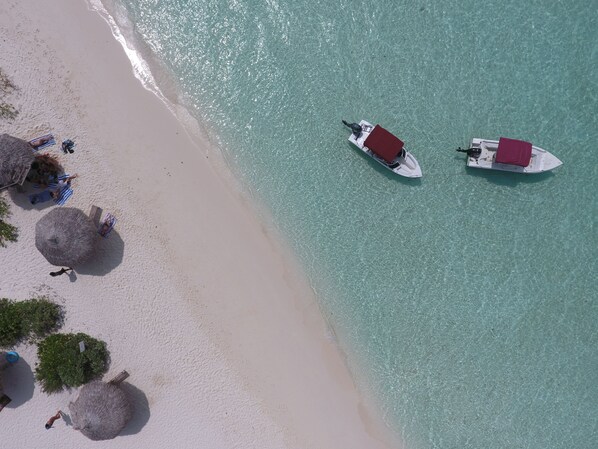 An aerial view of a beach with two boats, a sandy shore, and thatched umbrellas.