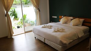 A neatly made bed with a quilted bedspread and pillows, a wooden floor, and a view of the outdoors through a sliding glass door.