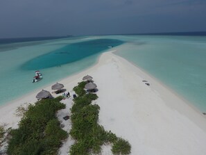 An aerial view of a beach with clear turquoise waters, a boat, and thatched-roof structures.
