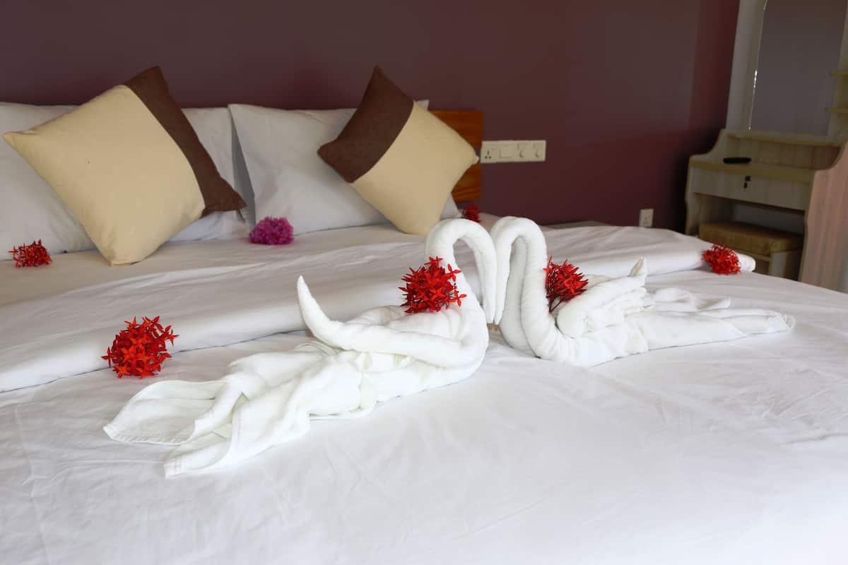 A neatly made bed with white linens, two pillows, and decorative swan-shaped towels with red flowers.