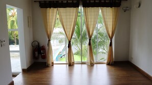 A room with a wooden floor, large windows with curtains, a ceiling fan, and a fire extinguisher on the wall.