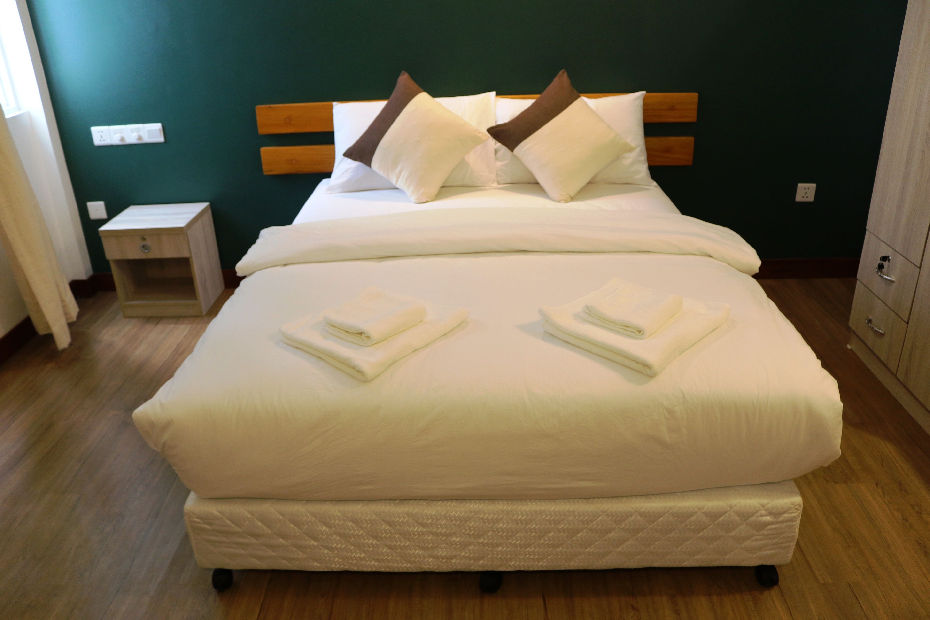 A neatly made bed with white bedding and two pillows, a wooden headboard, a small bedside table, and a nightstand.