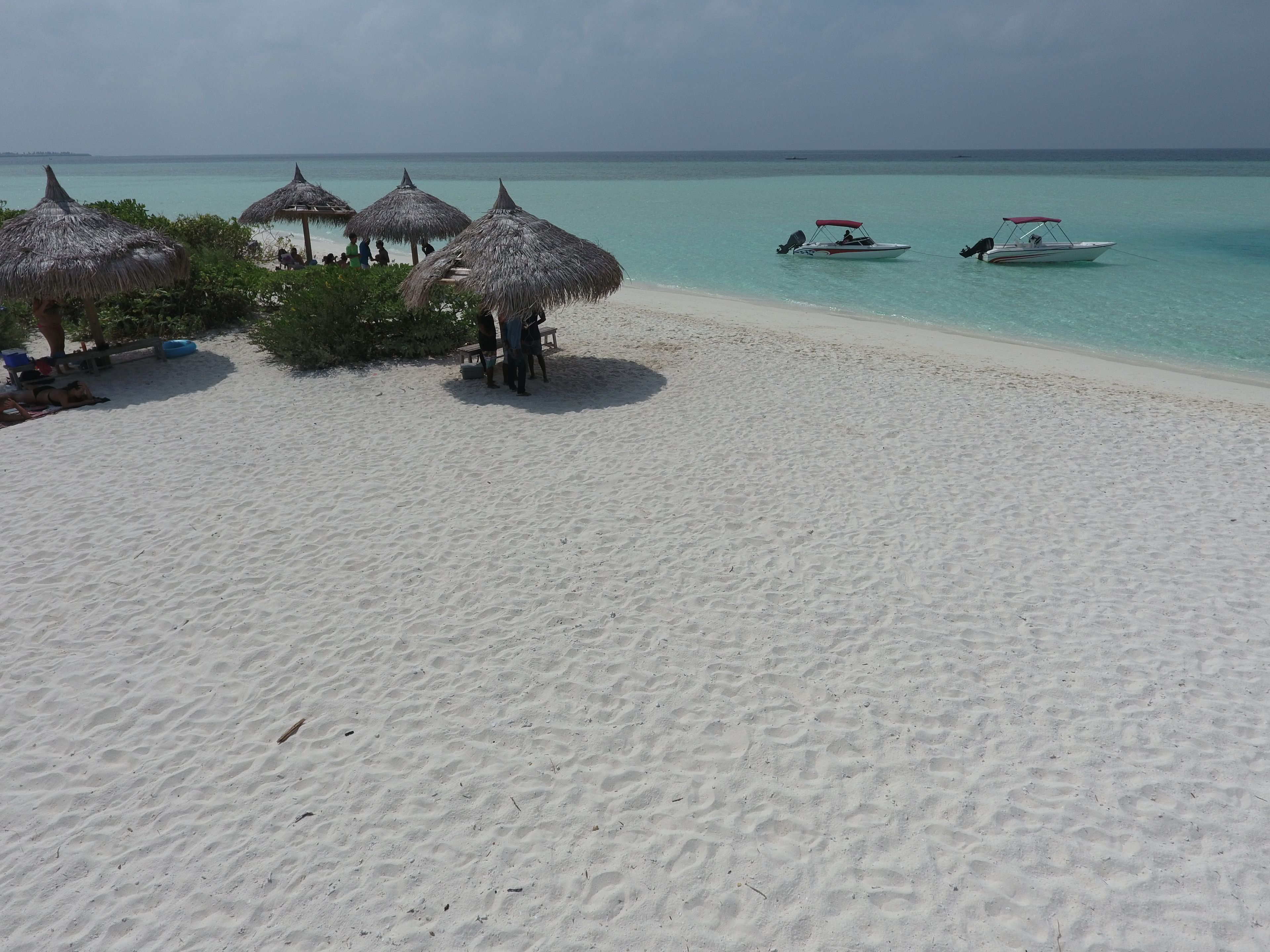 A beach with thatched umbrellas, a boat, and clear turquoise water.