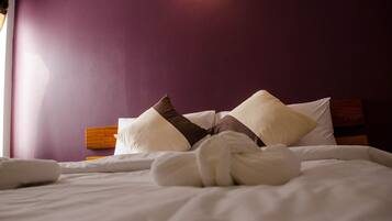 A neatly made bed with white linens and brown decorative pillows, set against a purple wall.