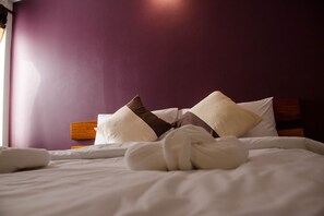 A neatly made bed with white linens and brown decorative pillows, set against a purple wall.