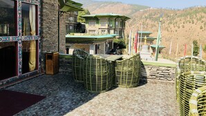 A traditional building with a stone facade, a balcony with a green roof, and a view of a mountainous landscape.