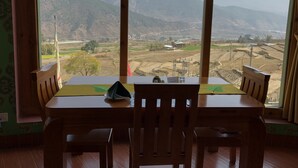 A dining table with chairs, a view of a mountainous landscape, and a window with a curtain.