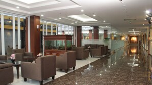A hotel lobby with a long corridor, seating area with sofas, a fish tank, and a reception desk. - Atrium Premiere Hotel Cilacap (Cilacap)