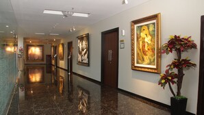 A polished hallway with marble flooring, framed artwork on the walls, and a potted plant. - Atrium Premiere Hotel Cilacap (Cilacap)