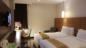A hotel room with two beds, a TV, a desk with a kettle and cups, and a chair. - Atrium Premiere Hotel Cilacap (Cilacap)