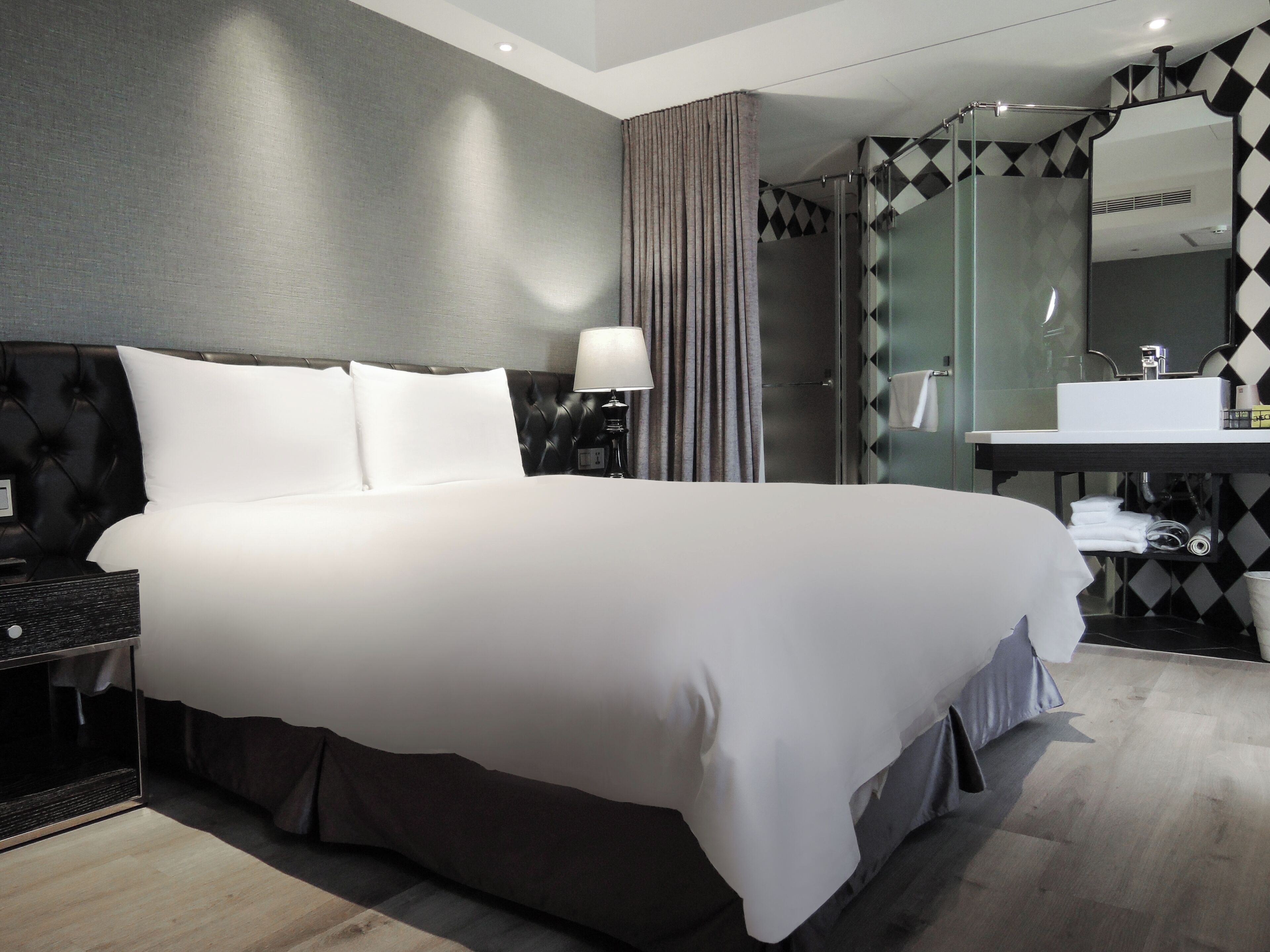 A hotel room with a large bed, a nightstand, a lamp, a bathroom with a mirror, and a sink.