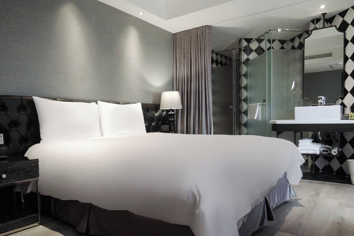 A hotel room with a large bed, a nightstand, a lamp, a bathroom with a mirror, and a sink.