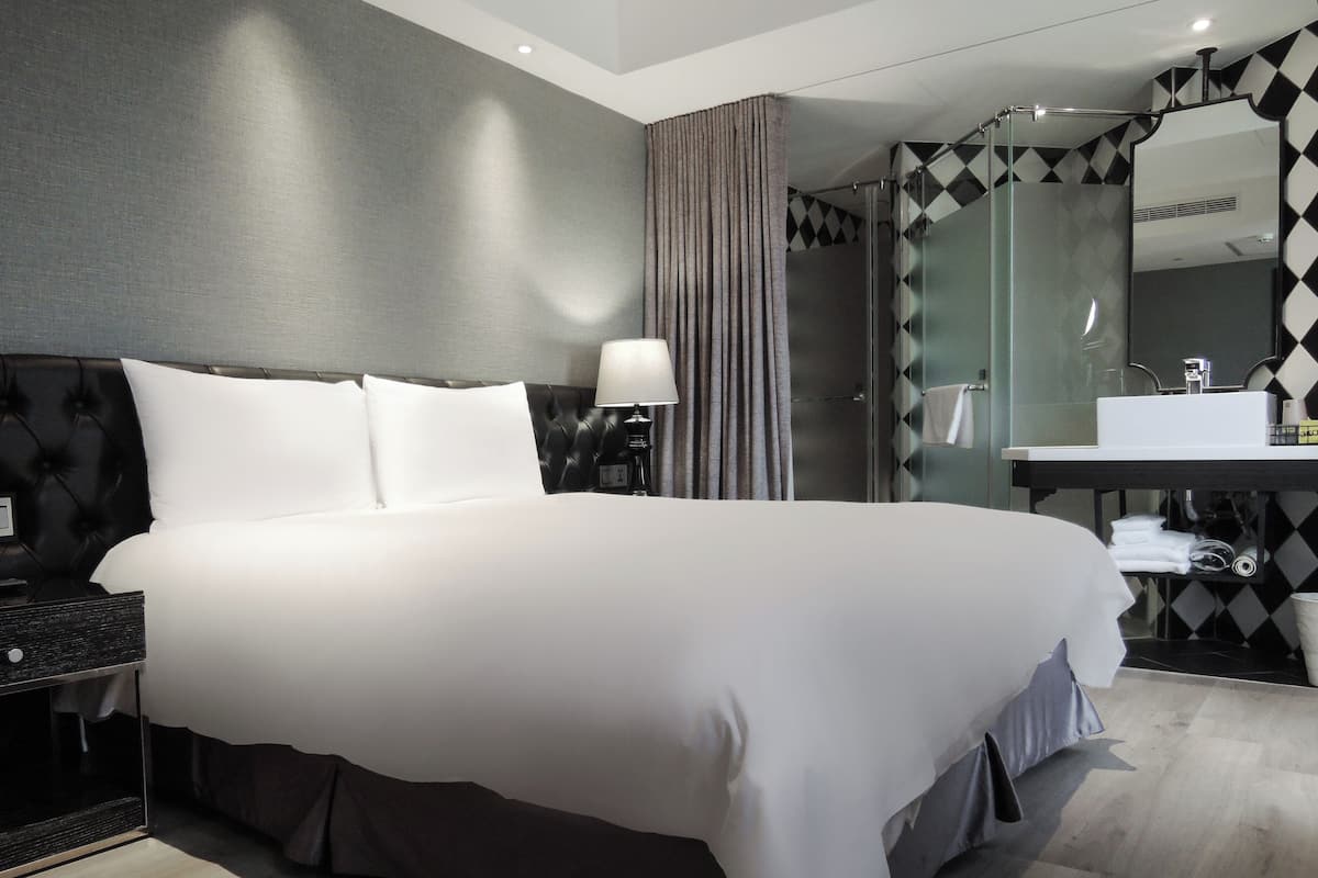 A hotel room with a large bed, a nightstand, a lamp, a bathroom with a mirror, and a sink.
