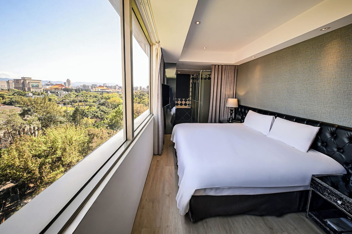 A modern hotel room with a large bed, a TV, a bathroom, and a city view.