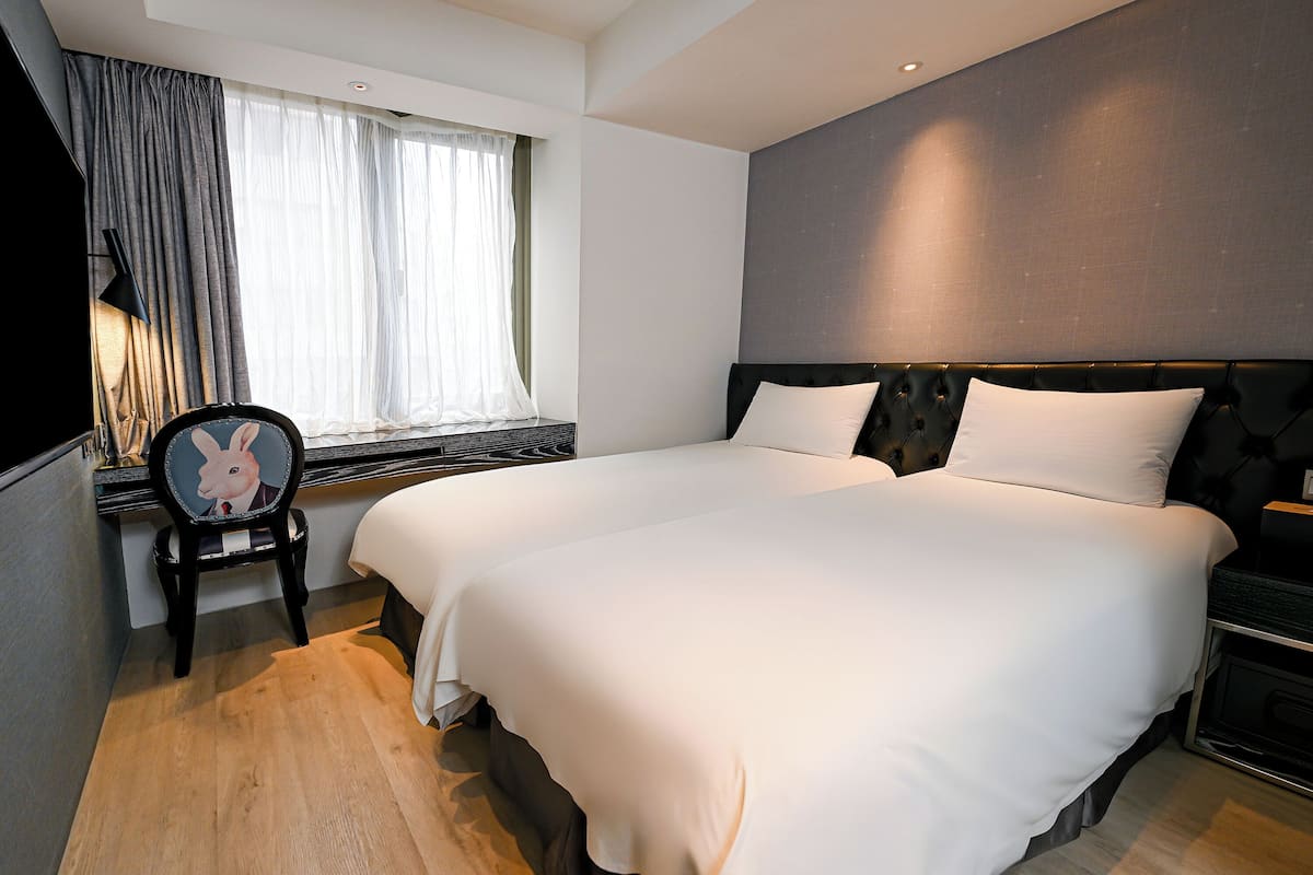 A modern hotel room with a large bed, a chair with a rabbit design, a window with sheer curtains, and a dark headboard.