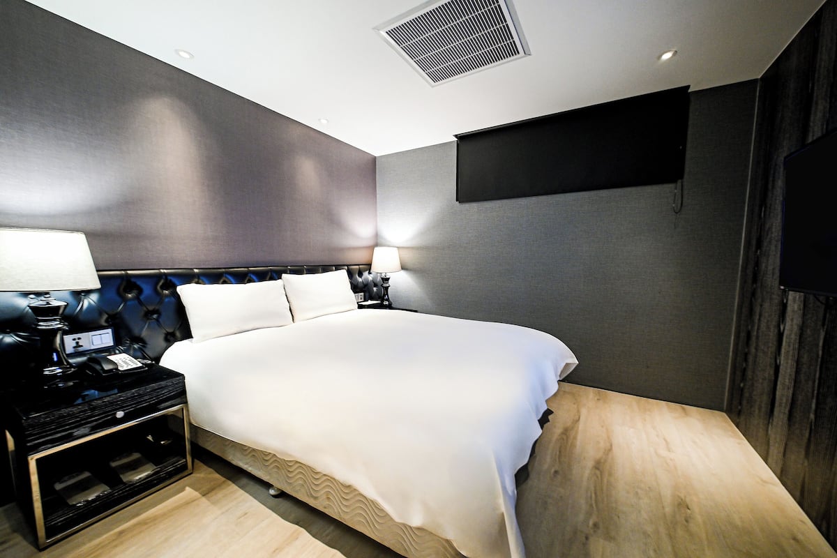 A modern hotel room with a large bed, bedside tables, a flat-screen TV, and a built-in air conditioning unit.