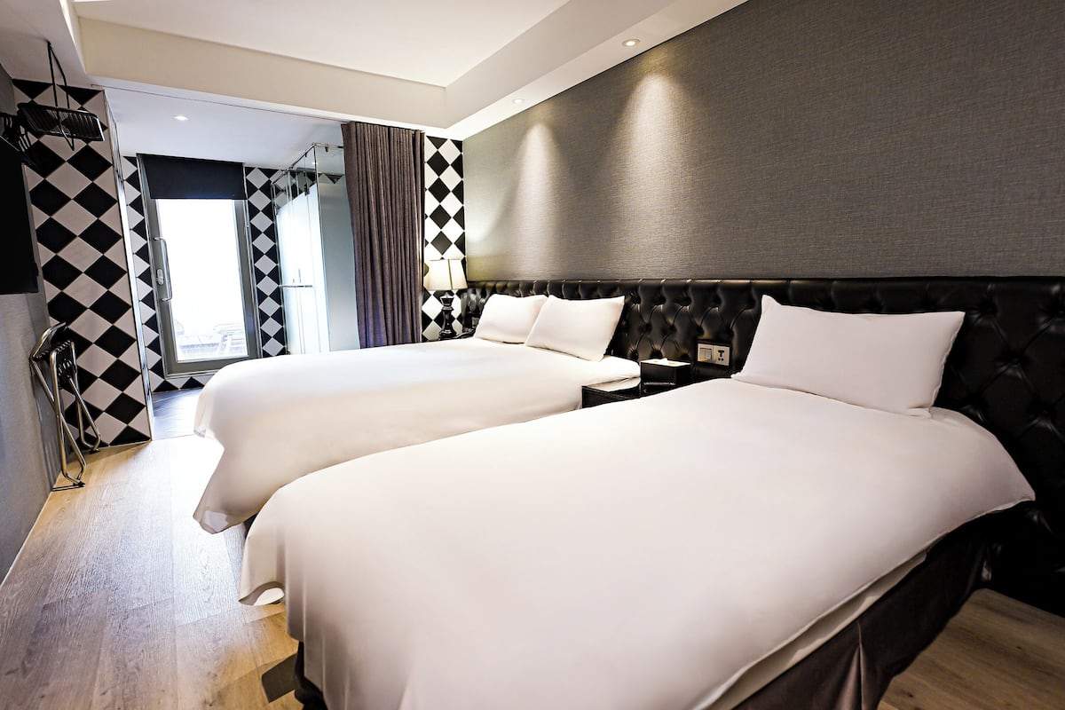 A hotel room with two beds, a modern design, a large window, and a check-in counter.