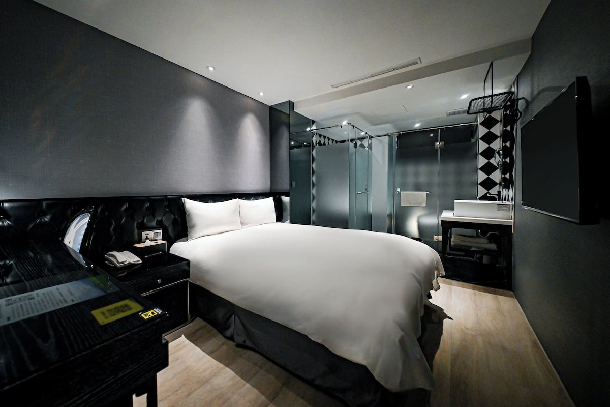 A modern bedroom with a large bed, a bedside table with a phone, and a mirror.
