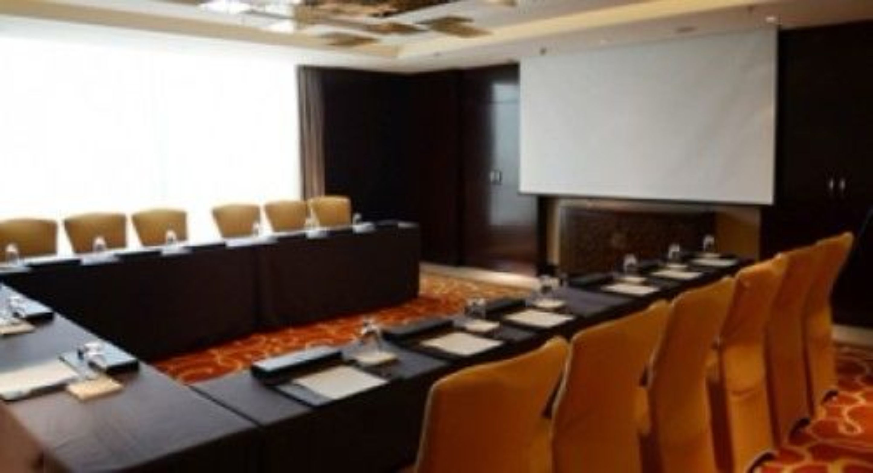 A conference room with a long table, chairs, a projector screen, and a fireplace.