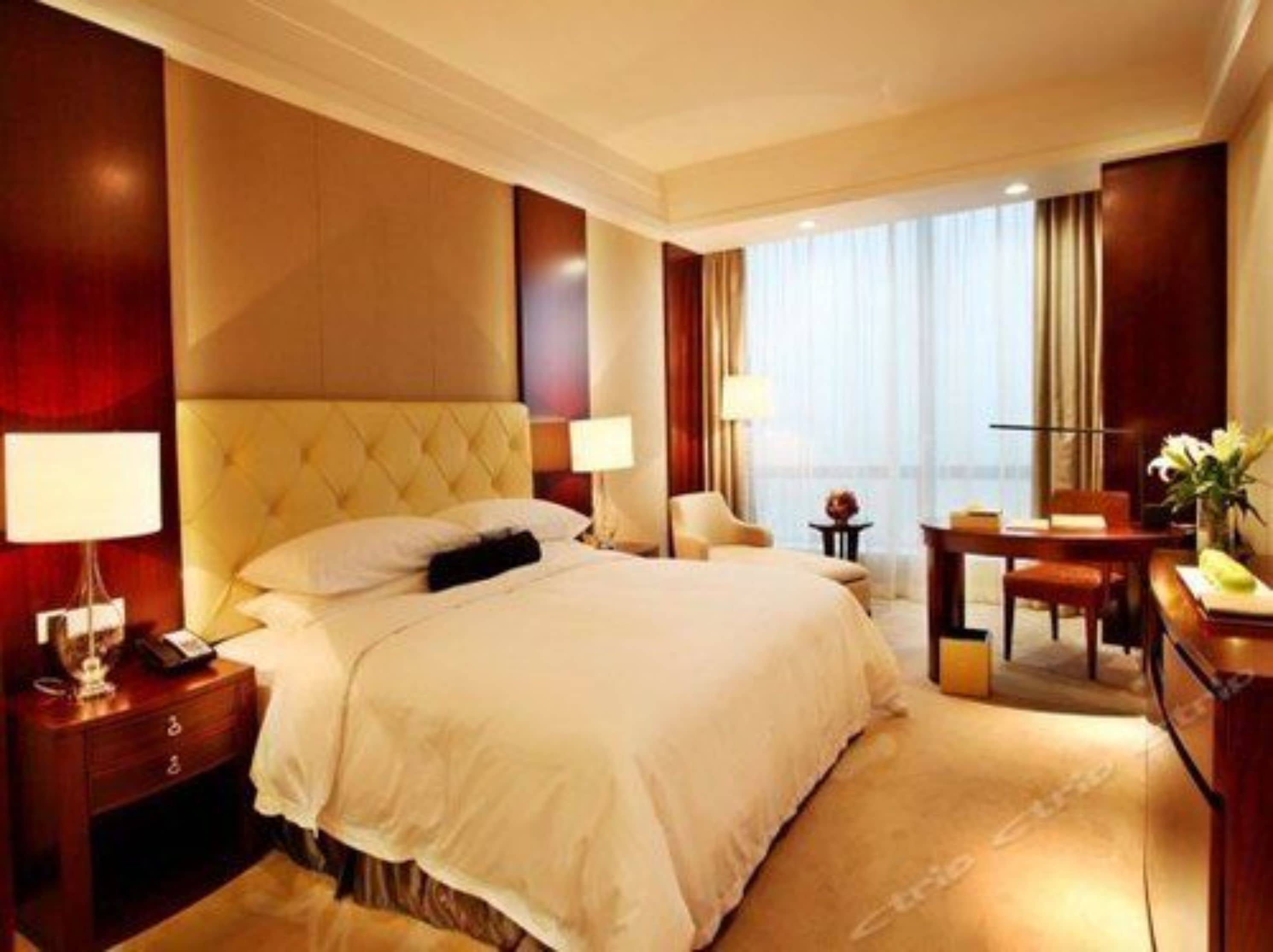 Habitación de hotel con una cama grande, un escritorio con silla, una lámpara y vistas a la ciudad a través de la ventana.