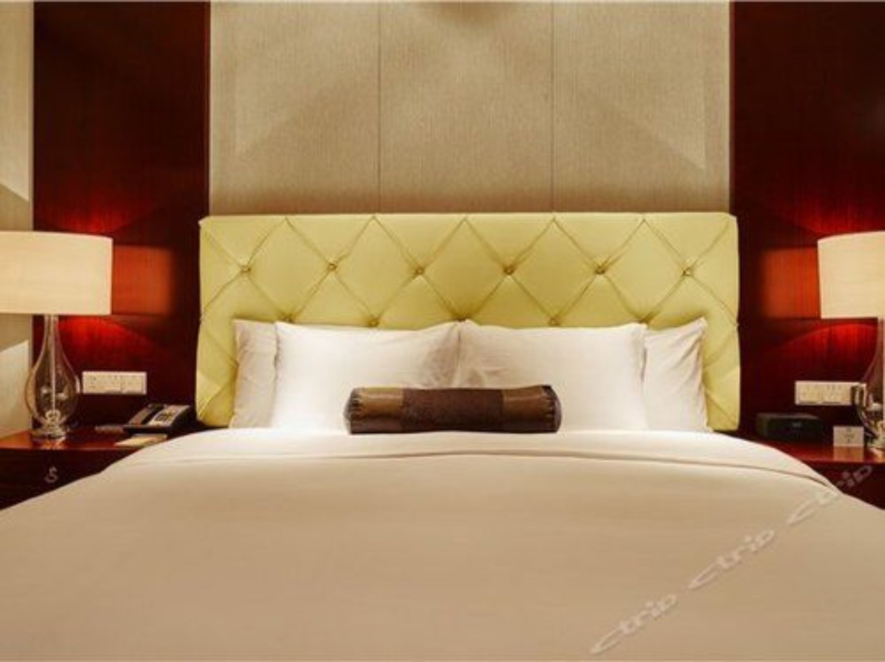 Quarto de hotel com cabeceira estofada, cama com lençóis brancos e duas luminárias laterais.