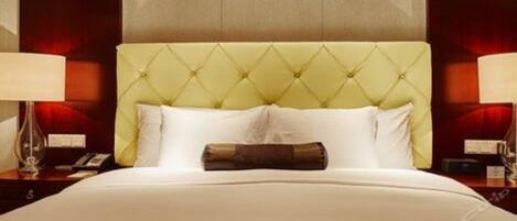 Quarto de hotel com cabeceira estofada, cama com lençóis brancos e duas luminárias laterais.