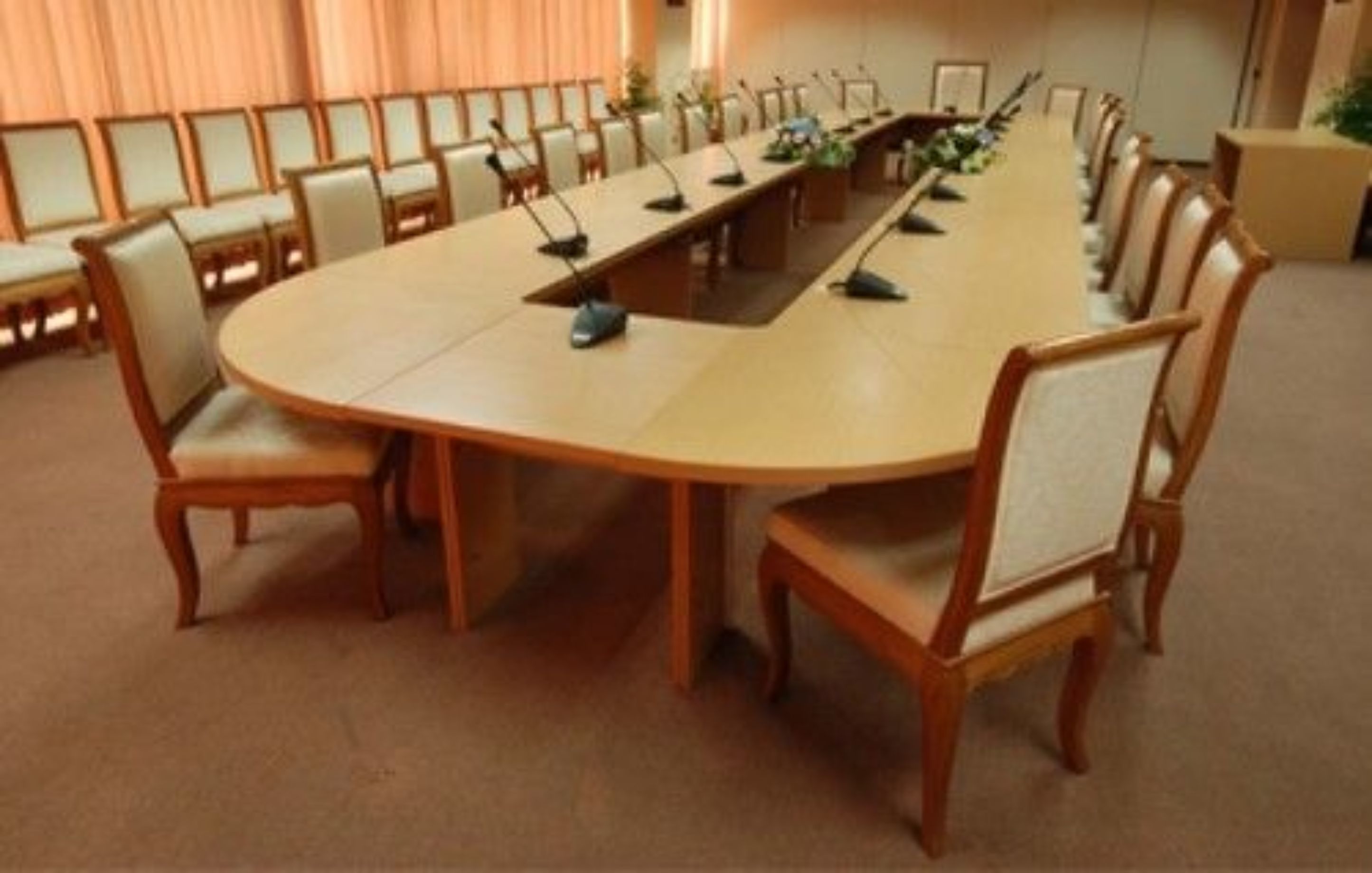 Una sala de conferencias con una larga mesa, sillas y micrófonos.