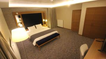 A hotel room with a large bed, a bedside table with a lamp, a desk with a chair, and a wardrobe.