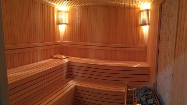 A sauna with wooden walls and benches, a wooden floor, and two wall-mounted lights. - Garden Zara Hotel (Zara)