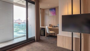 A modern hotel room with a large window, a flat-screen TV, a desk with a chair, and a small kitchenette. - Wallsun Hotel (Taipei)