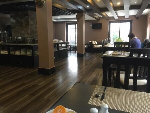 Un restaurant avec un sol, des tables et des chaises en bois. Une personne est assise à une table.