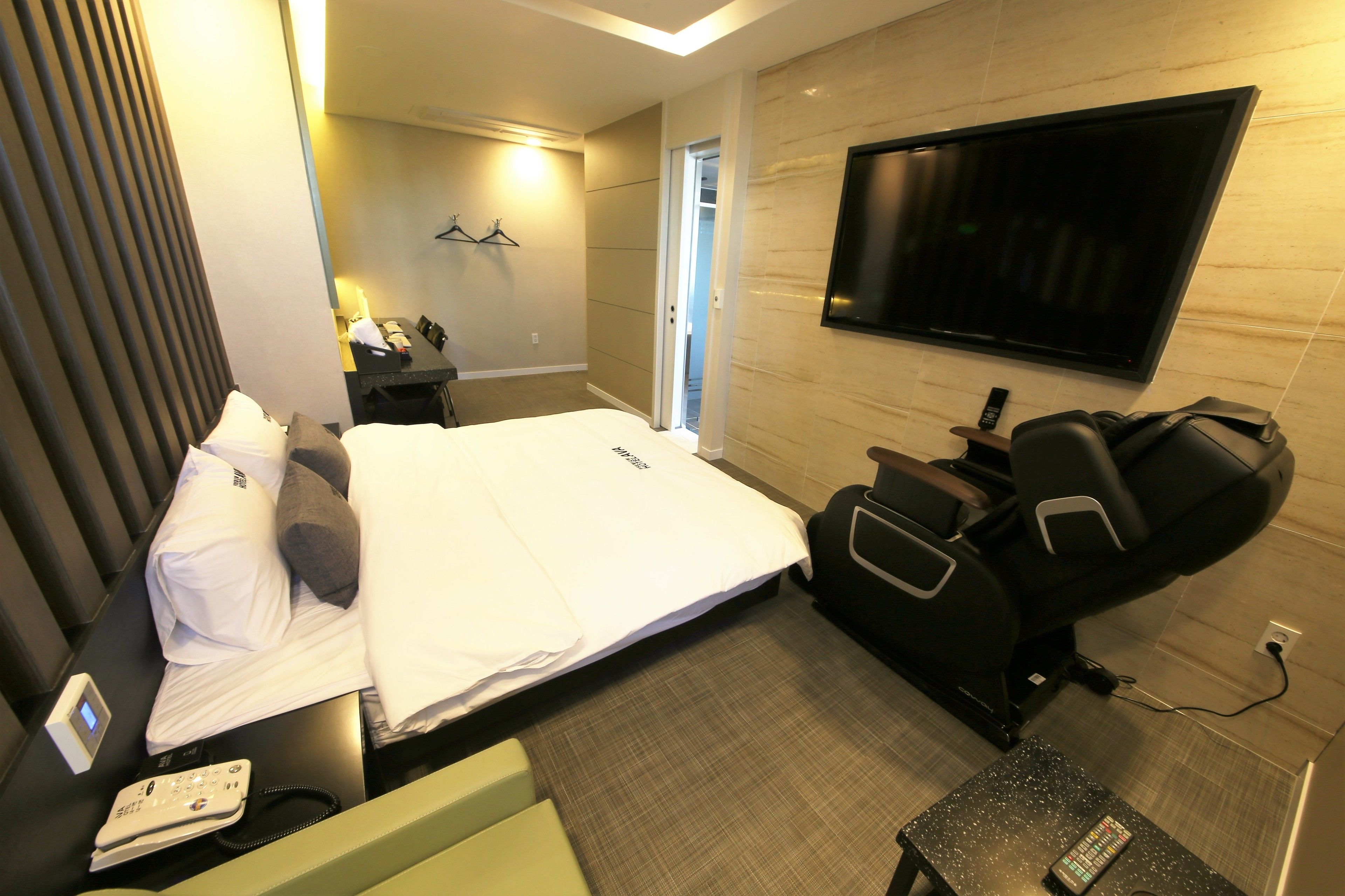 Une chambre d’hôtel équipée d’un lit, d’un fauteuil massant, d’une télévision, d’un bureau avec une lampe et d’une petite table avec une télécommande.